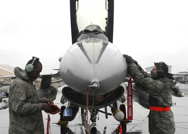 Airmen 1st Class Ronald Maynor (left) and Ryan Macz (right), both electrician/environmental specialist from the 455th Expeditionary Aircraft Maintenance Squadron, place the "remove before flight" reminders back on the F-16 Fighting Falcon, Dec. 10. These reminders are placed on the aircraft to remind the crew members to inspect the aircraft thoroughly. (Credit: 455th Expeditionary Air Wing 12/10/09)