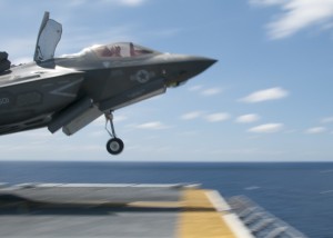 50522-N-BQ308-110 ATLANTIC OCEAN (May 22, 2015) As fast as its name, an F-35B Lightning II screams past a flight deck handler as it takes off during flight operations aboard the amphibious assault ship USS Wasp (LHD 1). Wasp, with VMFA-121 and VMFAT-501 embarked, is underway conducting the first phase of operational testing for the F-35B Lightning II aircraft, which will evaluate the full spectrum of F-35B measures of suitability and effectiveness in an at-sea environment. (U.S. Navy photo by Chief Mass Communication Specialist William Tonacchio/Released)
